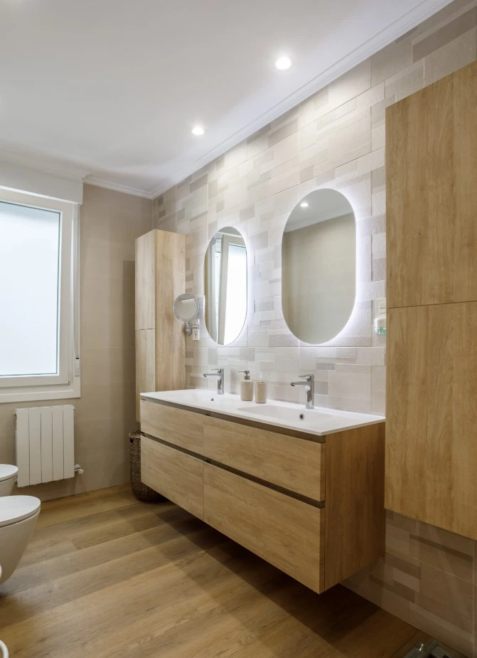 Reforma de baño con mueble suspendido de madera y espejos ovalados retroiluminados en Alicante